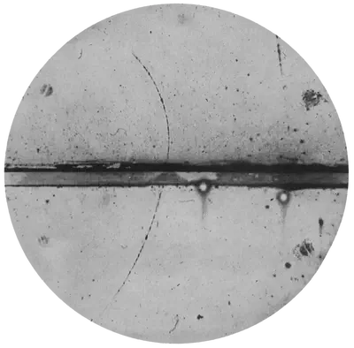 Imagen de la traza dejada por un [**positrón**](https://es.wikipedia.org/wiki/Positrón) en una [**cámara de niebla**](https://es.wikipedia.org/wiki/Cámara_de_niebla).  Sobre un círculo gris aparece una raya negra que la atraviesa de lado a lado con trazas describiendo un arco a lo largo de ella. Fuente: https://commons.wikimedia.org/wiki/File:PositronDiscovery.png